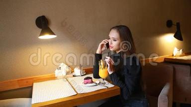 年轻女孩在电话里交谈，微笑着喝着刚榨的橙汁，吃着蓝莓芝士蛋糕